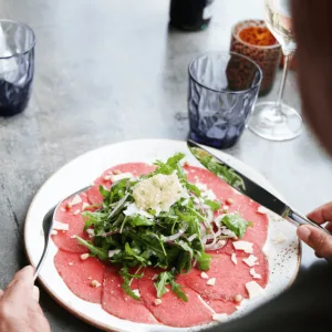 Carpaccio met rucola en kaasschilfers, gast met mes en vork aan tafel