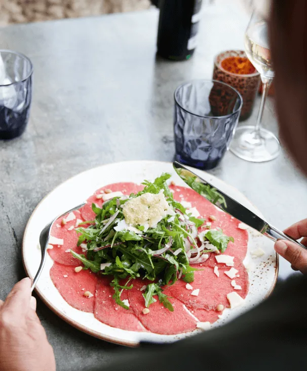 Carpaccio met rucola, rode ui en kaasschilfers op een bord