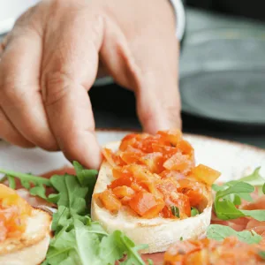 Hand neemt een bruschetta met tomaat van een bord met rucola