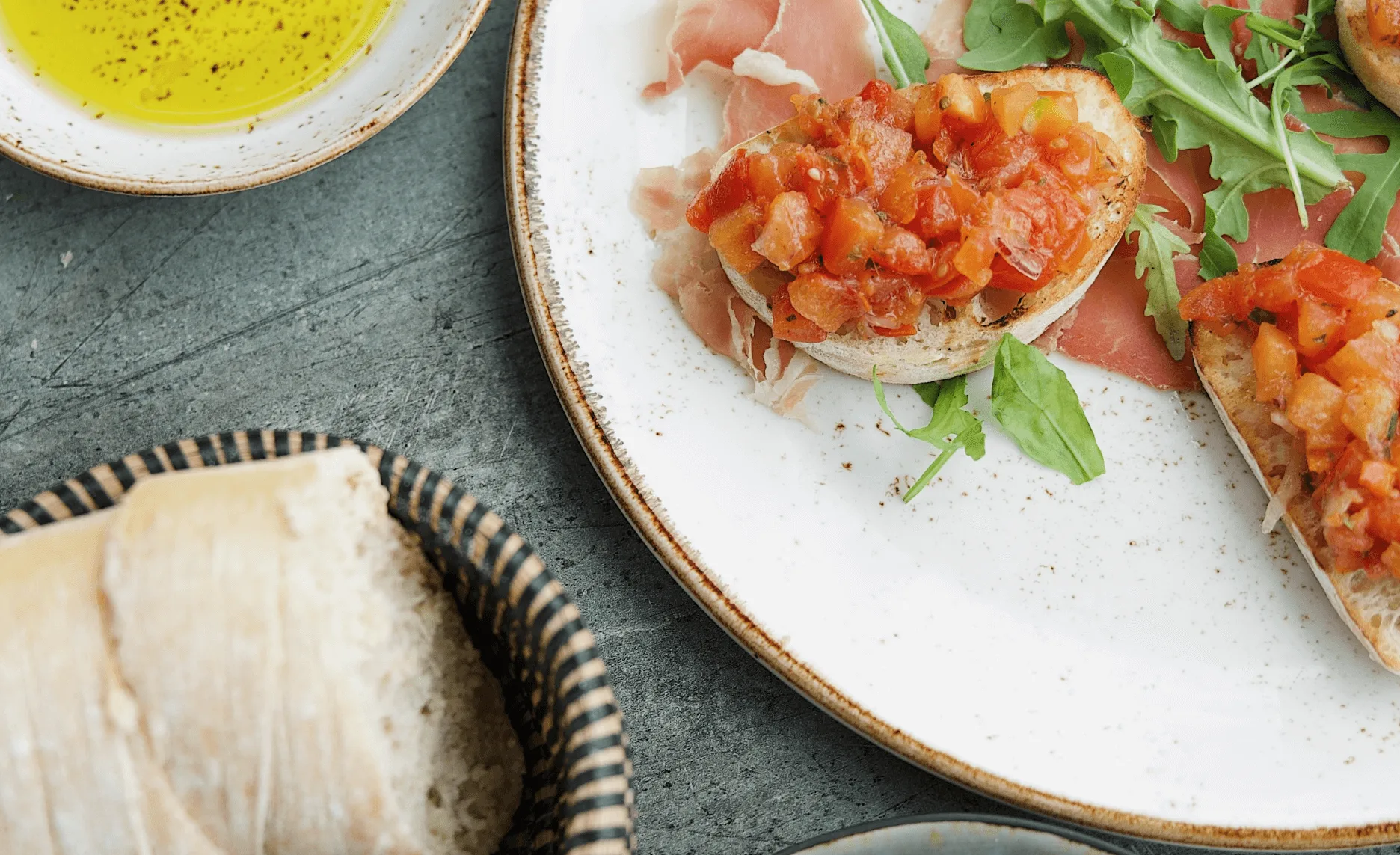 Bruschetta's met tomaat op rauwe ham en rucola, olijfolie en broodmandje ernaast