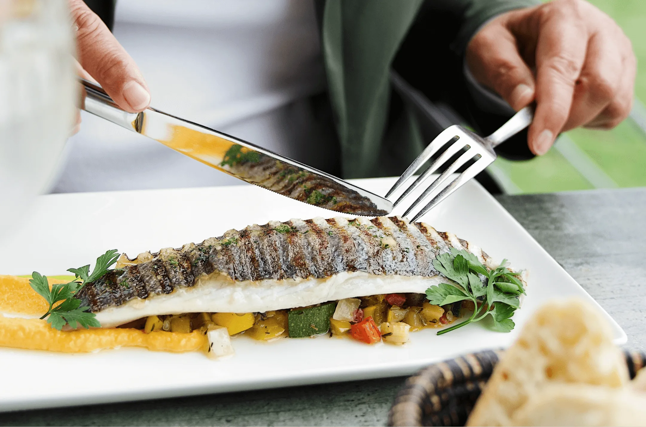 Gast snijdt in een gegrilde visfilet op blokjes groenten met oranje puree